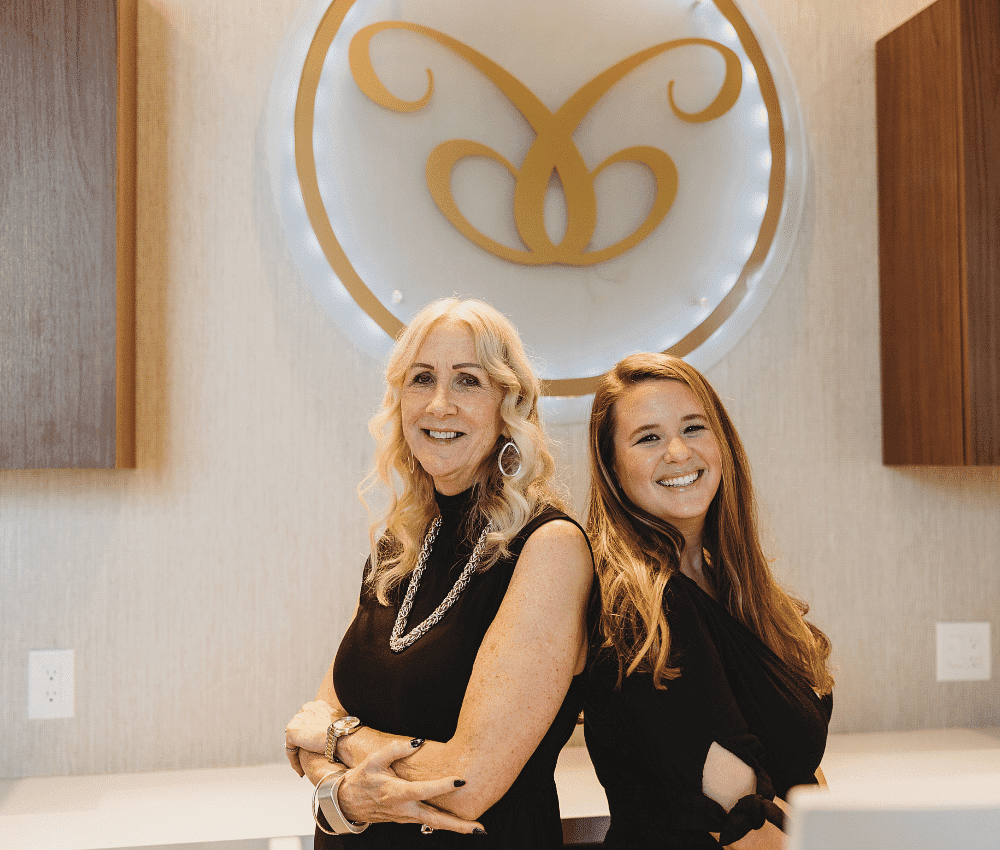 Two smiling women posing in front of a company logo.