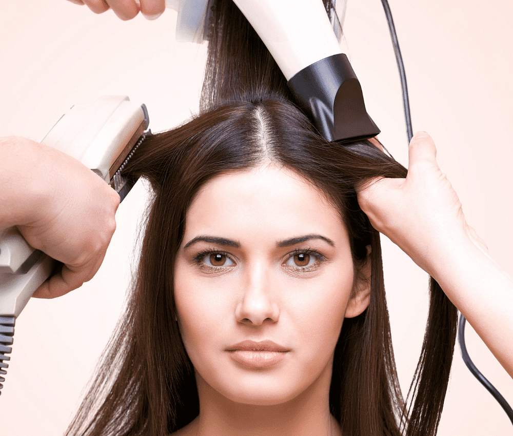 Woman getting hair styled with two hairdryers.